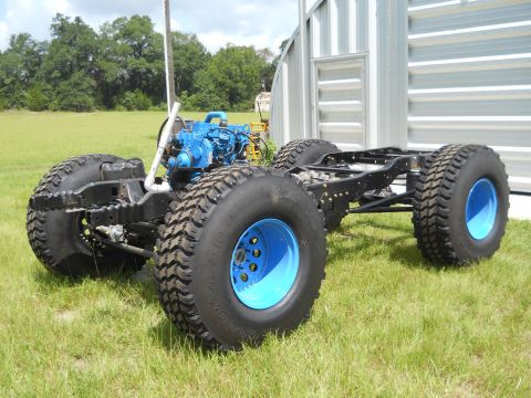 1992 Ford Bronco - This image shows a vehicle chassis with oversized tires and a prominent blue engine, set against a grassy backdrop.