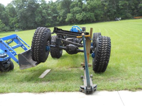 1992 Ford Bronco - A vehicle chassis with oversized tires is being worked on, with a tractor loader and a floor jack assisting.