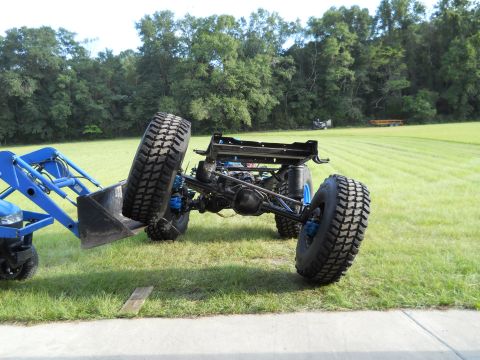 1992 Ford Bronco - A tractor loader is lifting the chassis of a vehicle with large off-road tires.