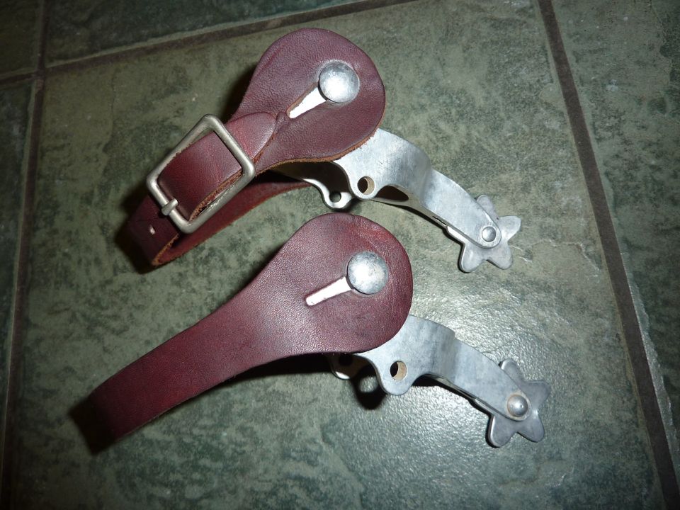 Two spurs with leather straps and metal buckles sit on a tiled floor