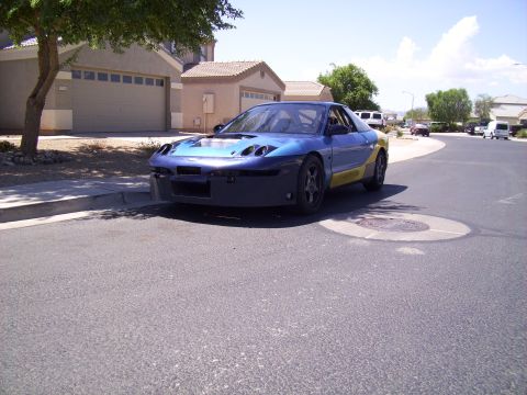 1995 Ford Probe - A modified blue and yellow race car is parked on a suburban street.
