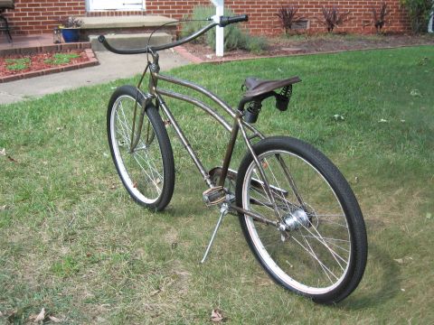 Brown custom cruiser bicycle with wide handlebars and a sprung seat, parked on grass