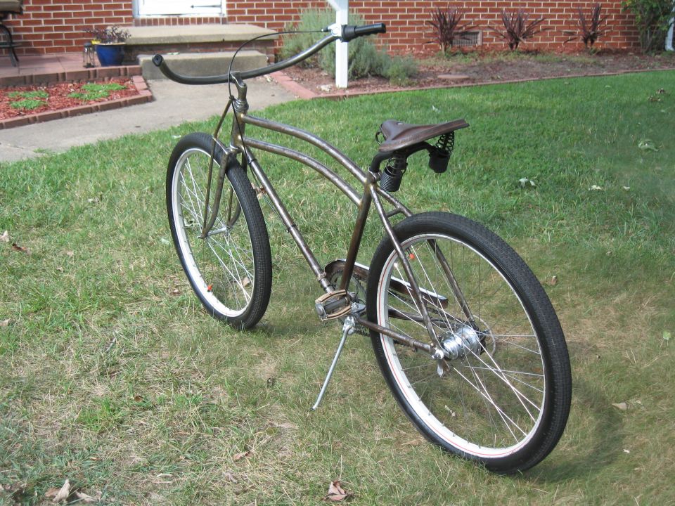 Brown custom cruiser bicycle with wide handlebars and a sprung seat, parked on grass