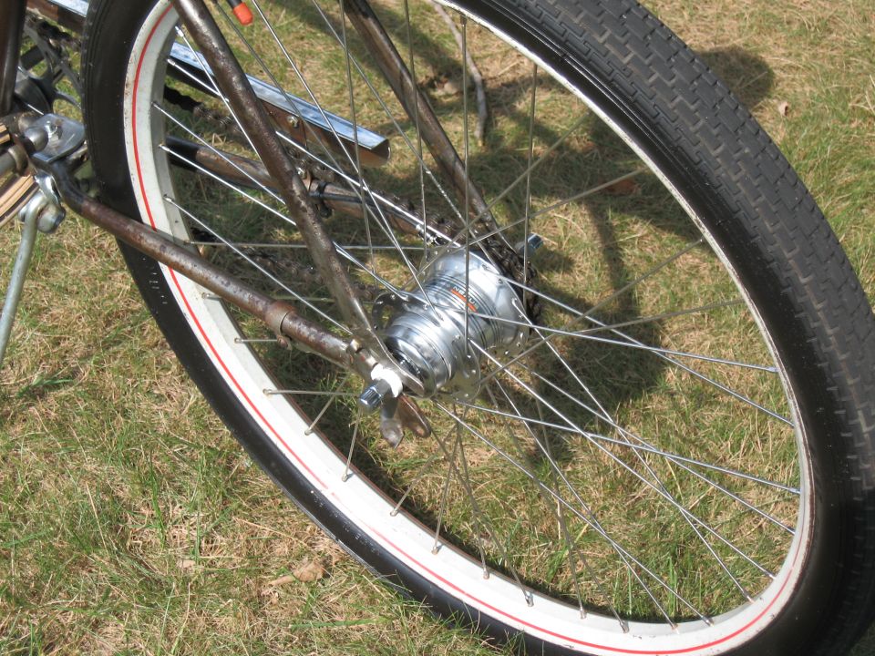 close-up of a bicycle's rear wheel with a shiny hub and spokes, set against a grassy background