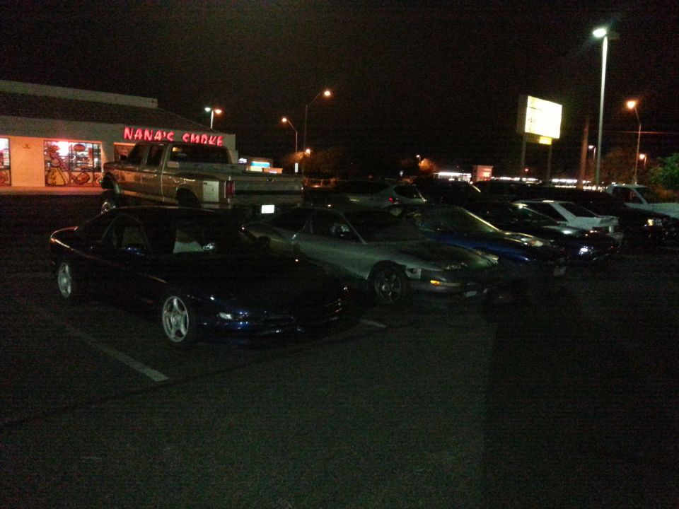 Dark blue Ford Probe parked at night, other cars and a pickup truck nearby