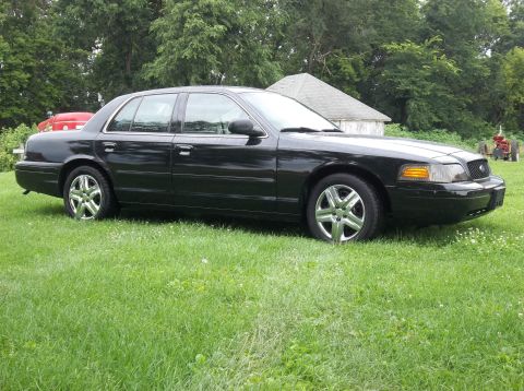 2006 Ford Crown Victoria - A black 2006 Ford Crown Victoria sedan is parked on a grassy lawn with a barn and tractor in the background.