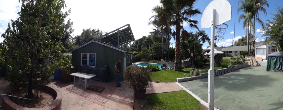 Backyard scene with a green shed, solar panels, swimming pool, and basketball hoop