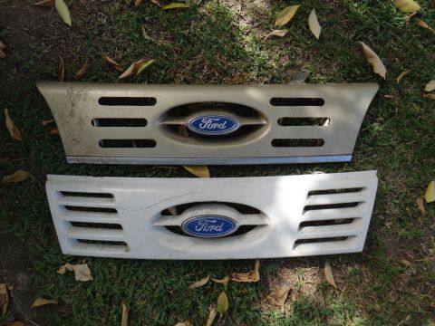 1995 Ford Taurus - Two Ford grilles, one gold and one white, are displayed on the grass.