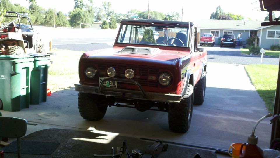 Red 1970 Ford Bronco parked in a driveway, front view. Aftermarket bumper and hood scoop visible