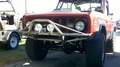 1970 Ford Bronco - This red SUV has a custom bumper and is parked next to a trailer with another vehicle.