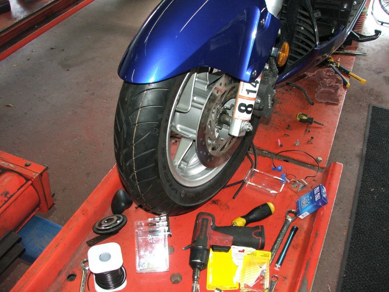 Motorcycle front wheel, brake disc, and caliper assembly on a red service tray with tools
