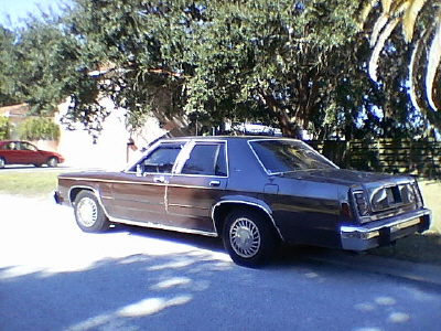 1987 Ford Crown Victoria LTD - A 1980s Ford Crown Victoria sedan is parked curbside, with a red car in the background.