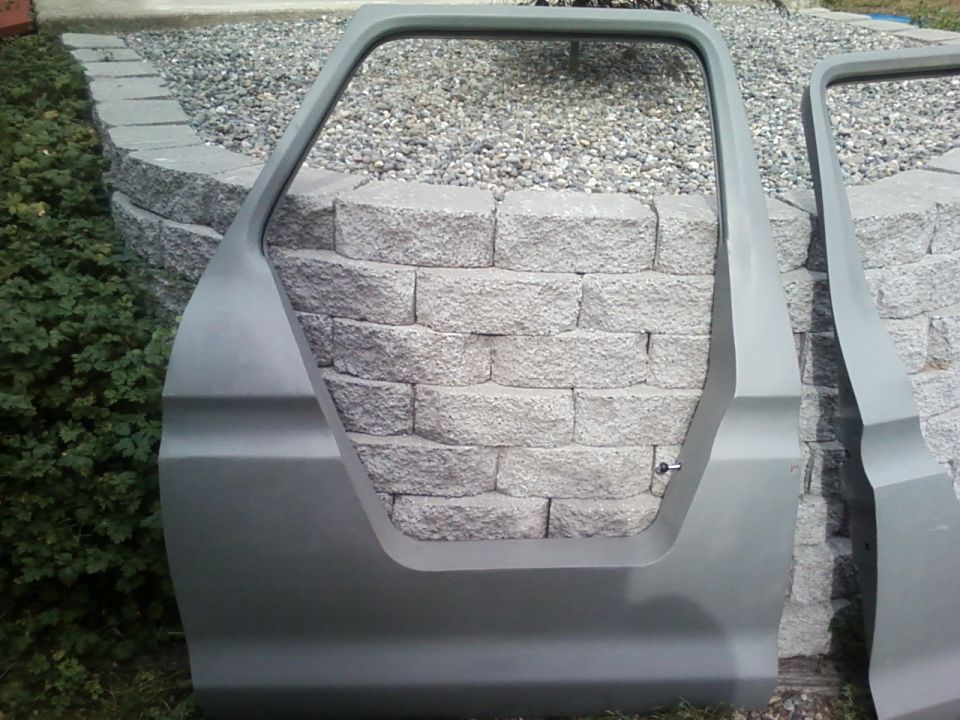 Two gray car doors, one in foreground, leaning against a stone wall