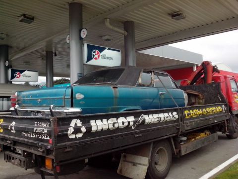 1969 Lincoln Continental - A blue sedan is loaded onto a flatbed truck, possibly for scrap, at a gas station with Texaco signage.