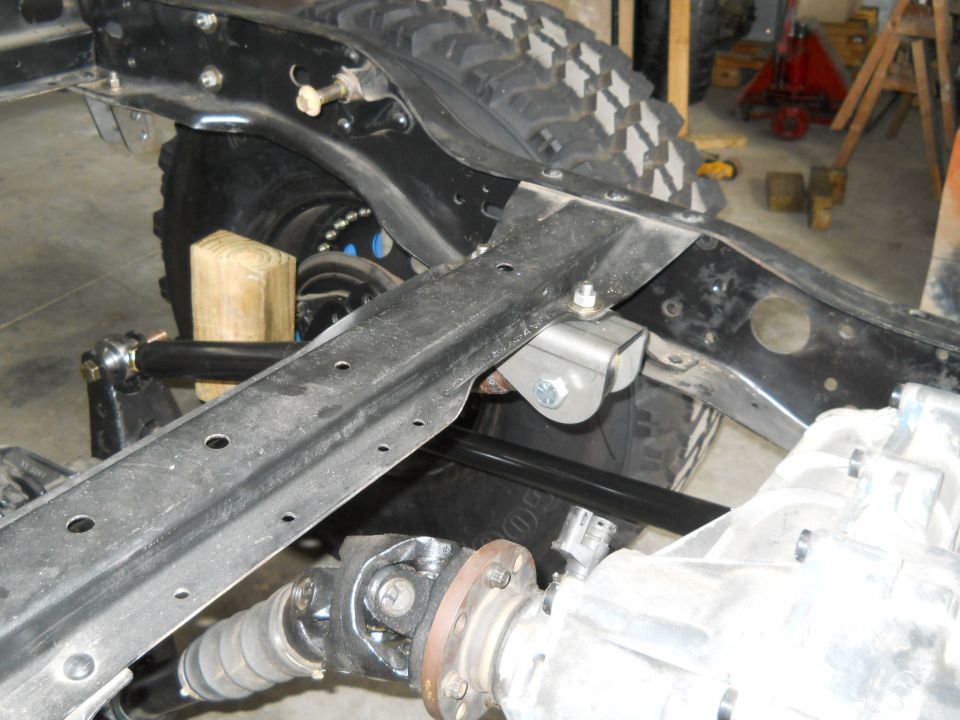 Close-up of vehicle frame with suspension and drivetrain parts visible. Supermotors.net logo in lower right