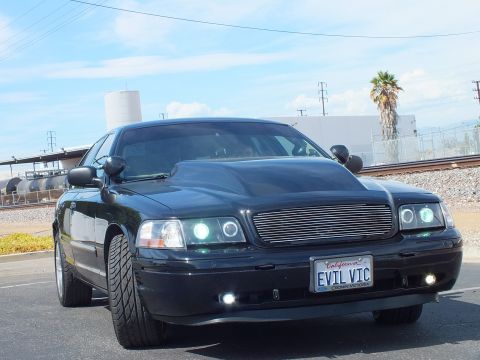 2003 Ford Crown Victoria - Front close-up of a black sedan showing a chrome billet grille, halo headlights and a California EVIL VIC license plate.