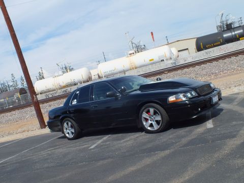 2003 Ford Crown Victoria - black sedan with red brake calipers and chrome wheels photographed at an angle beside railroad tracks and tank cars.