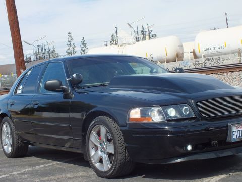 2003 Ford Crown Victoria - Close front three-quarter shot of a black sedan with chrome wheels, halo headlights and a partially visible EVIL VIC plate.