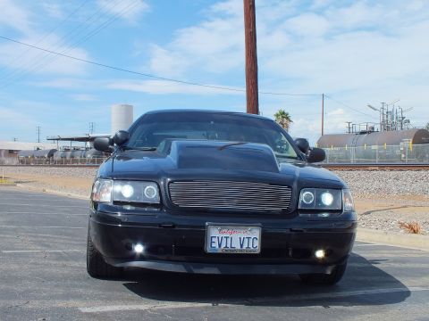 2003 Ford Crown Victoria - Head-on view of a black sedan with a billet grille, hood scoop and halo headlights, plate reading EVIL VIC, in a parking lot.
