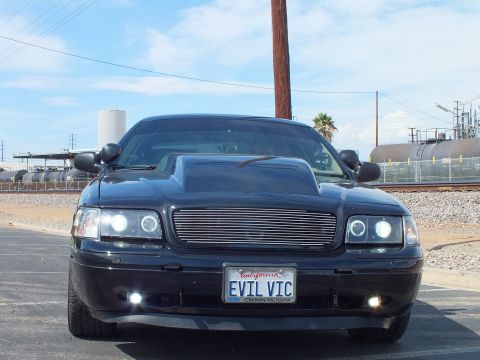 2003 Ford Crown Victoria - Head-on view of a black Ford Crown Victoria with a billet grille and halo lights; plate frame reads CROWN VICTORIA below an EVIL VIC plate.