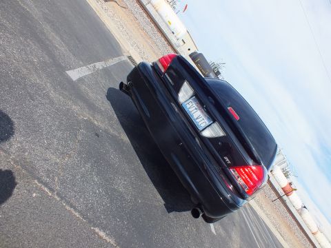 2003 Ford Crown Victoria - sideways-rotated photo showing the rear quarter of a black sedan with dual exhaust parked on pavement near railroad tracks.