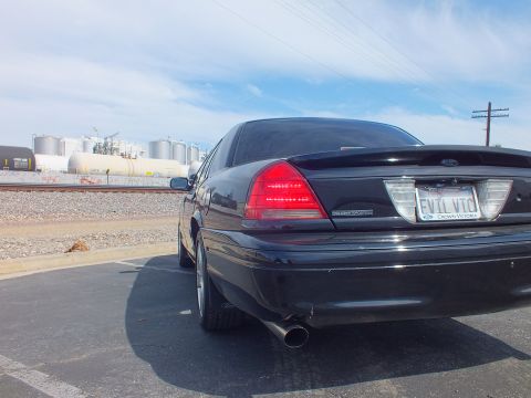 2003 Ford Crown Victoria - Rear three-quarter view of a black Ford Crown Victoria with chrome wheel, single exhaust and an EVIL VIC plate beside railroad tracks.