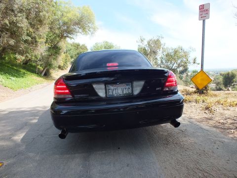 2003 Ford Crown Victoria - Direct rear view of a black sedan with dual exhaust tips and an EVIL VIC license plate on a wooded road.