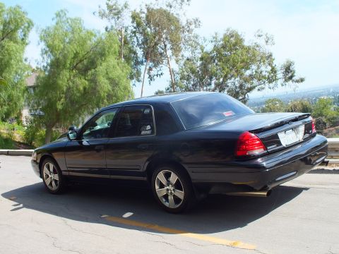 2003 Ford Crown Victoria - black full-size sedan with chrome five-spoke wheels and a trunk spoiler shown rear three-quarter among trees.