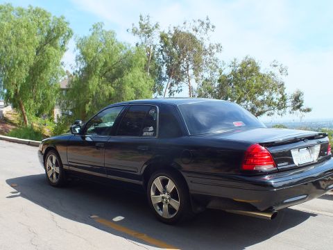 2003 Ford Crown Victoria - Rear three-quarter of a black full-size sedan with chrome wheels and a trunk spoiler on a curving overlook road.