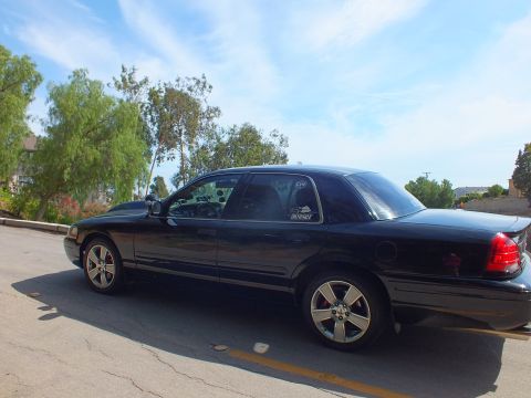 2003 Ford Crown Victoria - Driver-side profile of a black full-size sedan with chrome five-spoke wheels and red brake calipers.