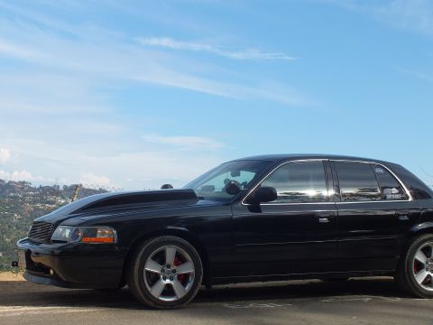 2003 Ford Crown Victoria - Front driver-side view of a black sedan with a cowl hood, billet grille, and red brake calipers at an overlook.