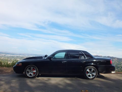 2003 Ford Crown Victoria - Driver-side profile of a black full-size sedan with chrome five-spoke wheels and red brake calipers at an overlook.