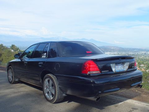 2003 Ford Crown Victoria - black Ford Crown Victoria sedan parked on a hilltop road, viewed from the rear three-quarter with a hazy valley and mountains behind.