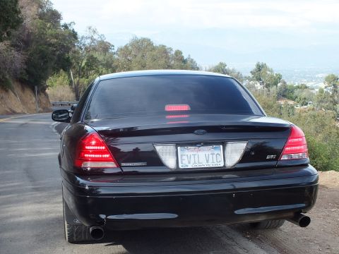2003 Ford Crown Victoria - Rear view of a black Ford Crown Victoria sedan on a winding road, showing the 'EVIL VIC' plate and a glowing center brake light.