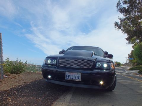 2003 Ford Crown Victoria - Front view of a customized black Ford Crown Victoria with a chrome billet grille, illuminated halo headlights, and an 'EVIL VIC' plate.