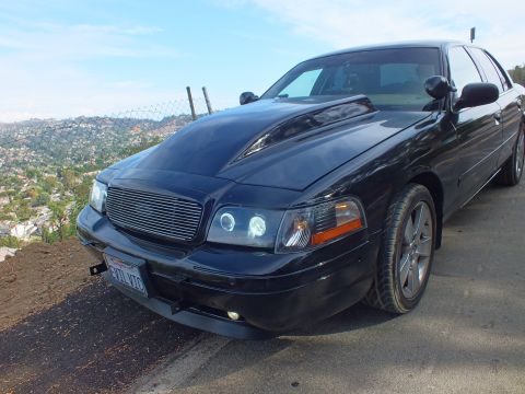 2003 Ford Crown Victoria - Front three-quarter view of a customized black Ford Crown Victoria with billet grille and halo headlights parked at a hilltop overlook.