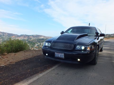 2003 Ford Crown Victoria - customized black Ford Crown Victoria seen from the front three-quarter, billet grille and halo lamps, parked on a hilltop road.