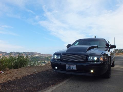 2003 Ford Crown Victoria - customized black Ford Crown Victoria viewed from the front three-quarter, billet grille and halo headlights, under a clear blue sky.