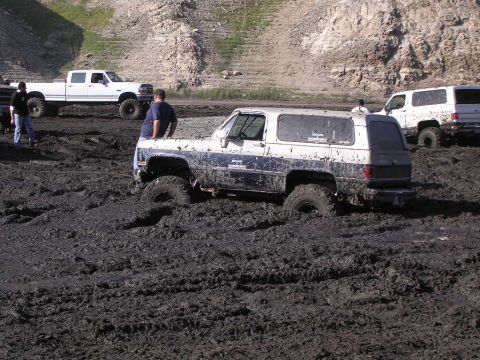 1985 Ford Bronco - Several off-road vehicles are stuck in deep mud during an apparent off-roading event.