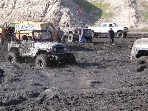 1985 Ford Bronco - Multiple off-road vehicles are stuck in a muddy terrain, with people observing the situation.