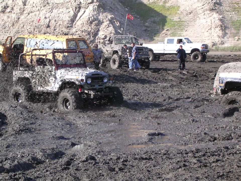 White mud-splattered lifted 4x4 SUV on big tires driving through deep mud at an off-road park