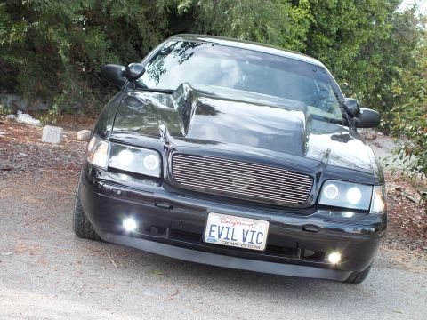 2003 Ford Crown Victoria - Low-angle front view of a black Ford Crown Victoria showing its cowl hood, billet grille, fog lamps and EVIL VIC plate.