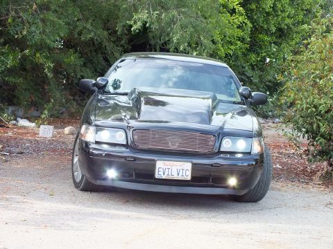 2003 Ford Crown Victoria - black customized full-size sedan photographed head-on, showing a cowl-induction hood, billet mesh grille, projector headlights, and a Calif…