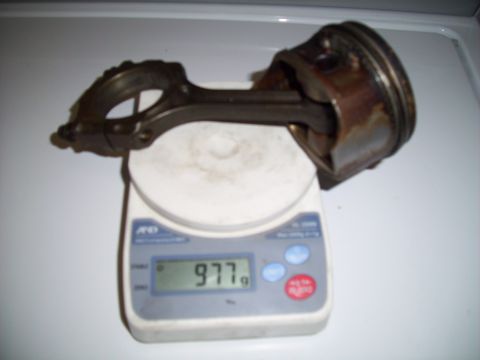 1995 Ford Probe - A piston and connecting rod assembly is weighed on a digital scale, showing a reading of 977 grams.