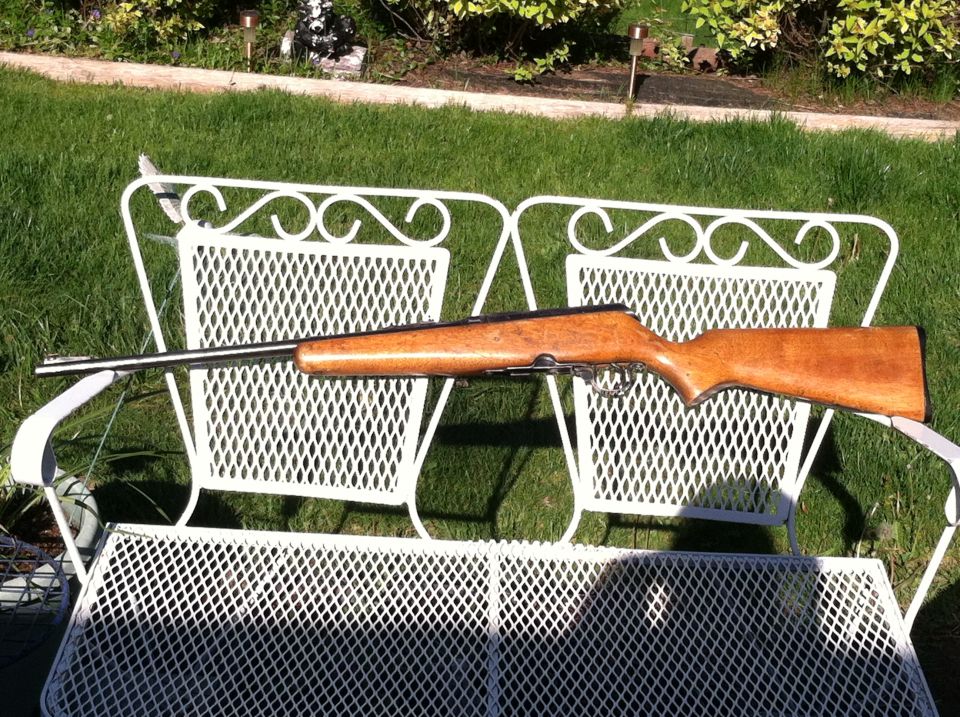 Rifle with wooden stock and metal barrel resting on a white metal bench outdoors