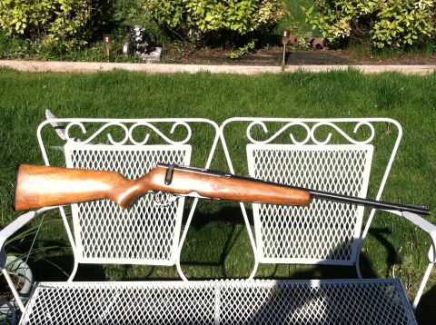 1989 Ford Bronco - A rifle is displayed outdoors on a white metal bench in front of a grassy lawn and bushes.