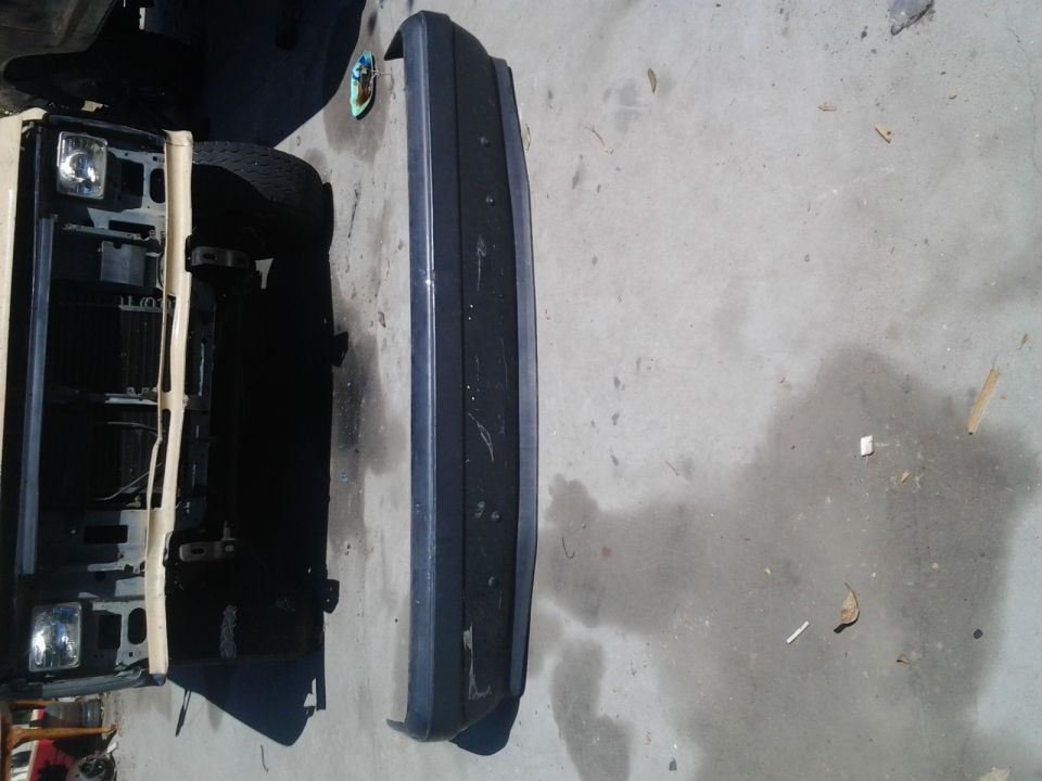 Tan Ford Bronco front end with headlights and grille removed, next to a dark bumper