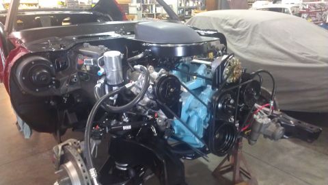 1972 Pontiac Trans Am - The engine bay of a car in restoration, with a blue engine and black hood scoop, is visible with another car covered in the background.