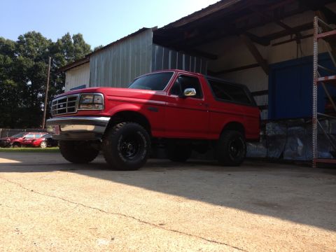 1992 Ford Bronco - This red 1992 Ford Bronco features a lifted suspension and off-road tires, parked in front of a building.