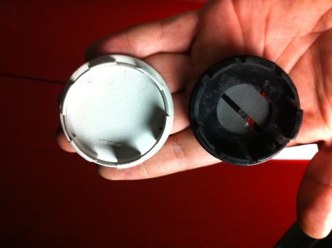 1995 Ford Mustang - A hand holds two wheel center caps, one white and one black, against a red background.